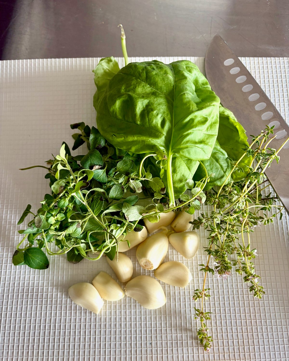Photo of fresh herbs and peeled garlic cloves on a white cutting board.