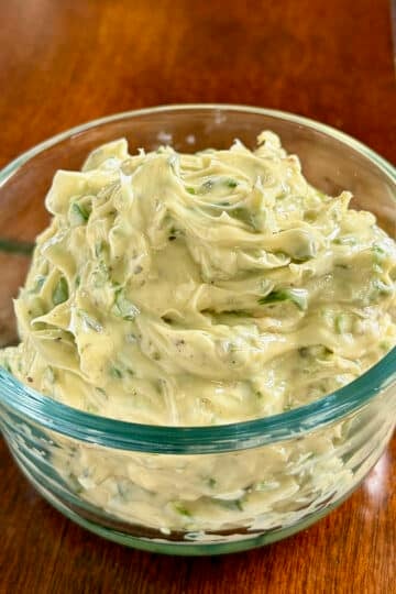 Close up photo of soft, spreadable Garlic Herb Butter in a clear glass serving bowl.