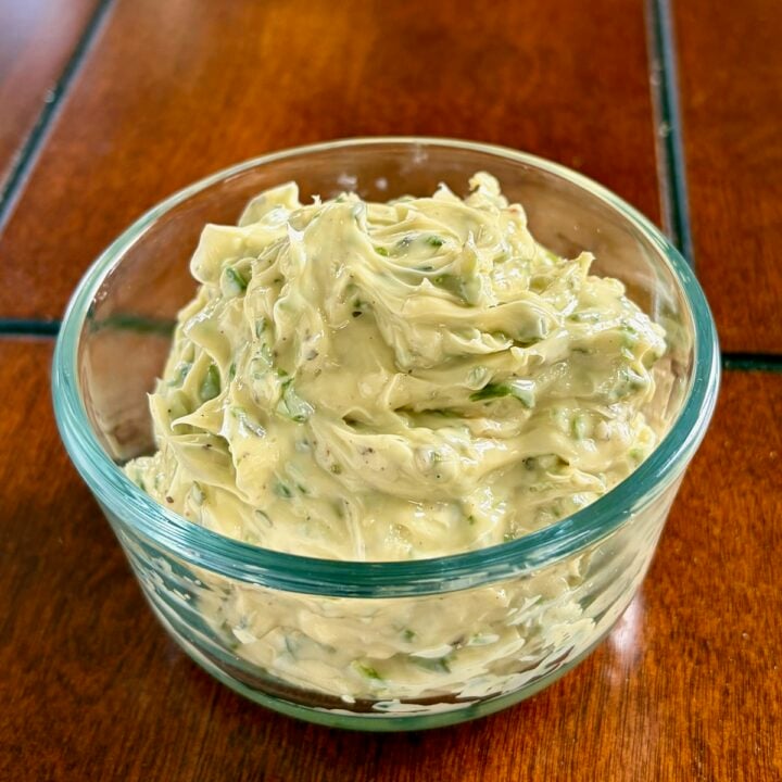 Close up photo of soft, spreadable Garlic Herb Butter in a clear glass serving bowl.
