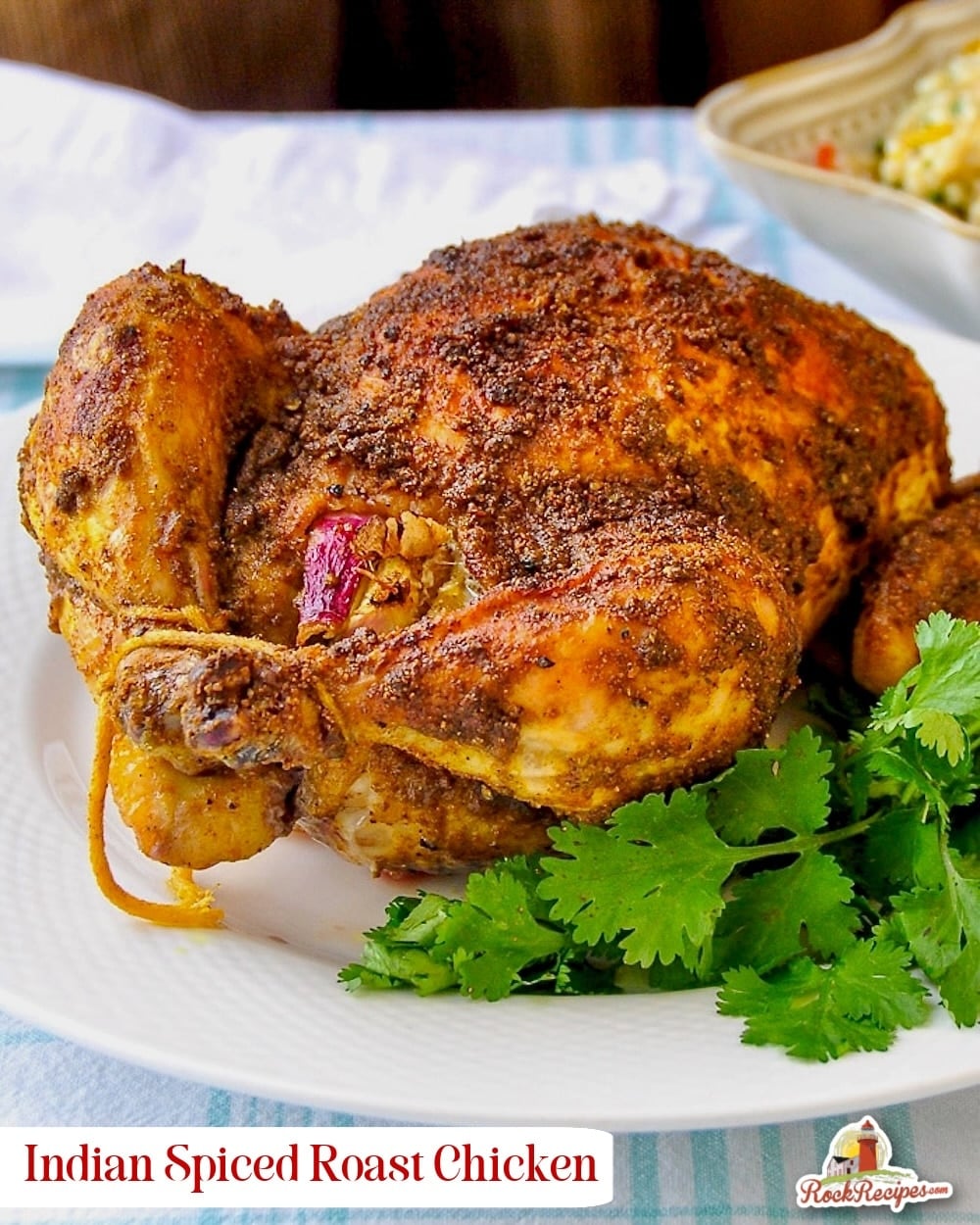 Indian Spiced Roast Chicken pictured on a white plate with fresh coriander leaves with title text added for social media posts.