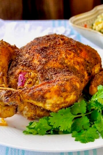 Indian Spiced Roast Chicken pictured on a white plate with fresh coriander leaves.