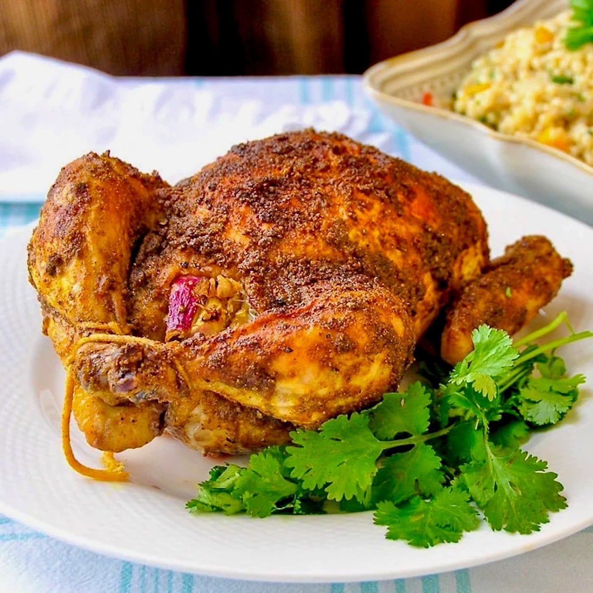 Indian Spiced Roast Chicken pictured on a white plate with fresh coriander leaves.