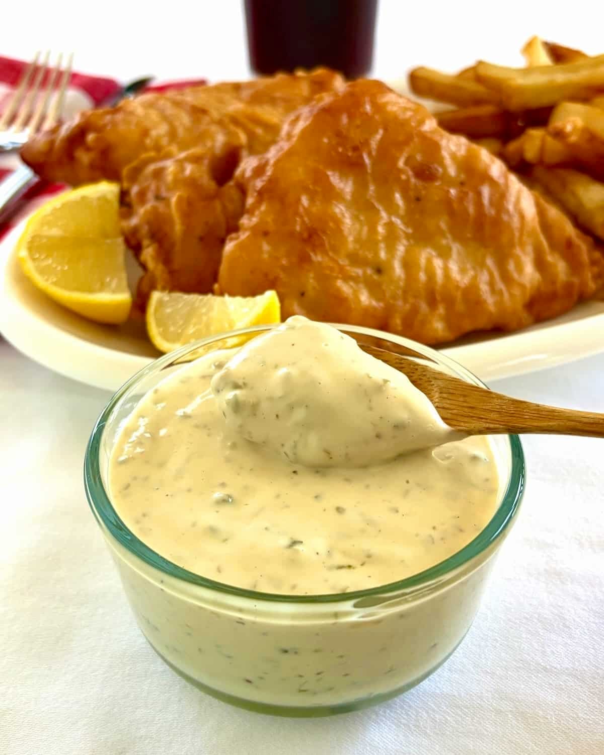 Photo of Lime Caper Tartar Sauce in a clear glass bowl with fish and chips in background