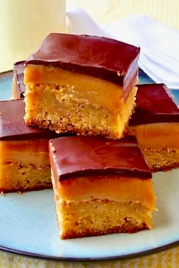 Millionaire Blondies photo of 5 cookie bars stacked on a blue plate with a glass of milk in the background.