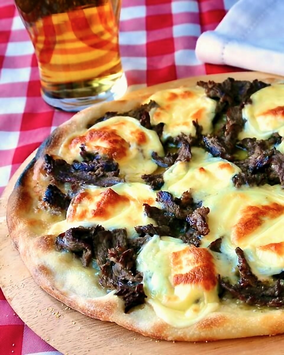 Philly Cheesesteak Pizza shown uncut in a wooden pizza peel with a glass of beer in the background.