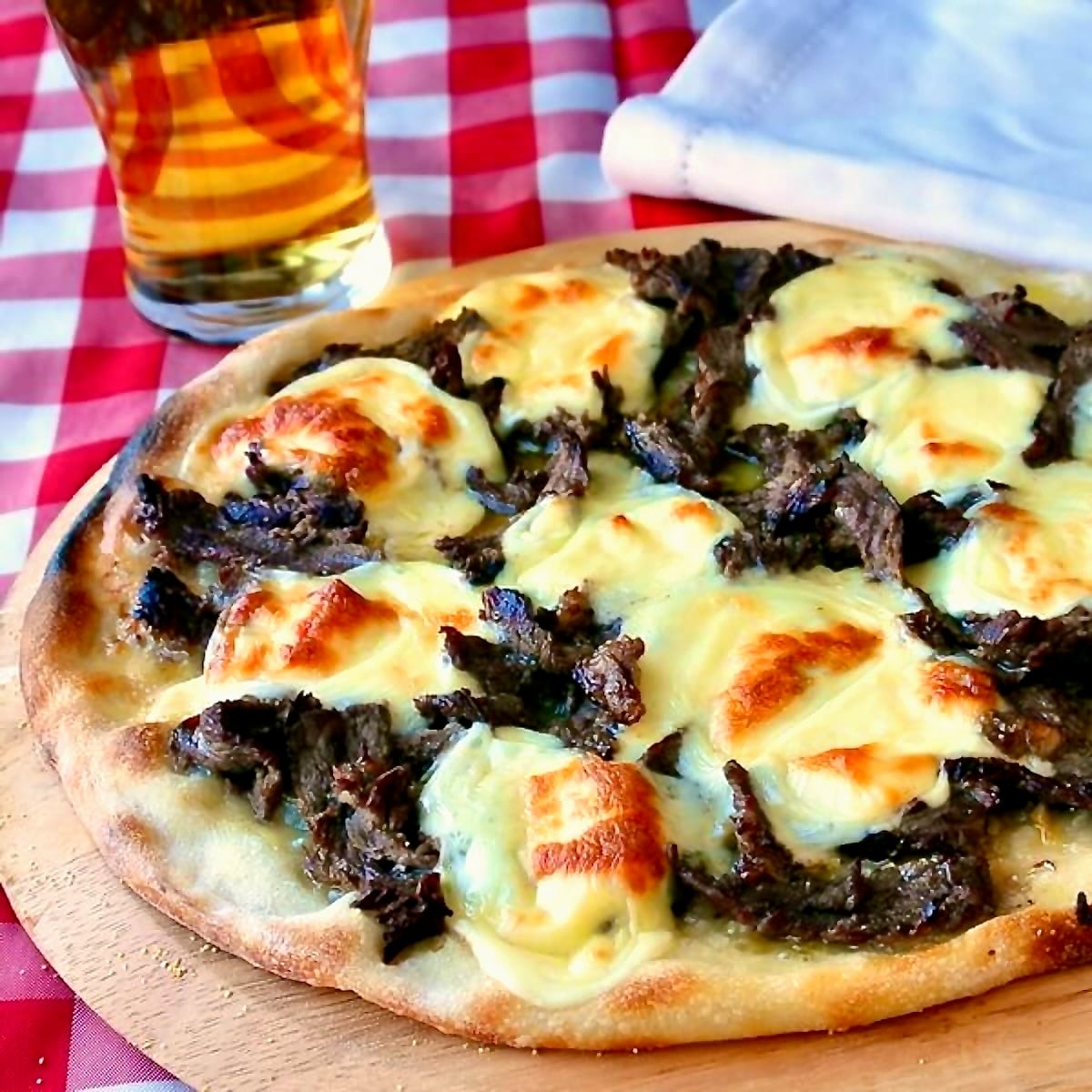 Philly Cheesesteak Pizza shown uncut in a wooden pizza peel.
