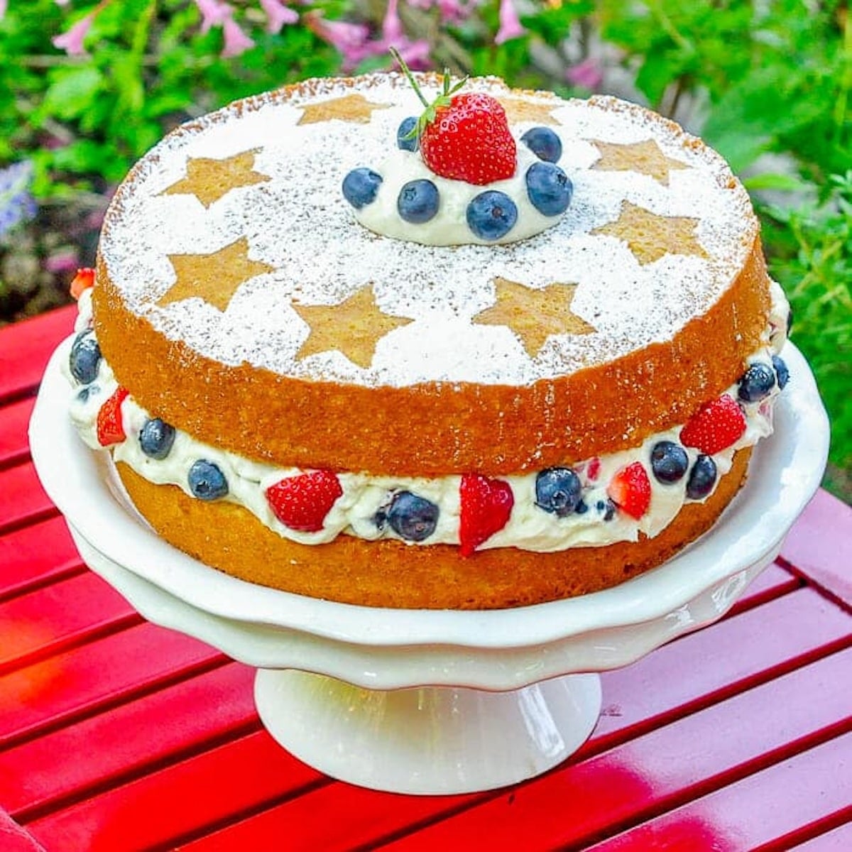 Red White & Blue Cake with Mascarpone Cream wide outdoors shot of finished cake on white pedestal stand.