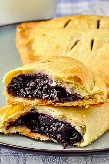 Blueberry Turnovers on a blue plate with milk in the background cracked in half to show filling.