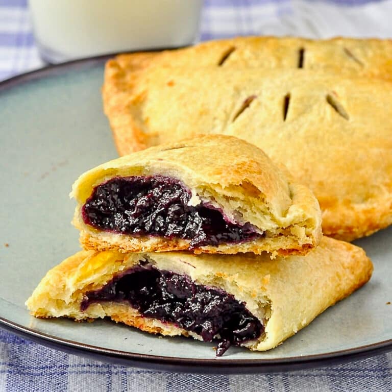 Blueberry Turnovers on a blue plate with milk in the background cracked in half to show filling.