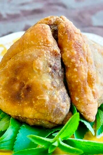 The Best Beef Samosas photo of garnished samosas on a yellow plate.