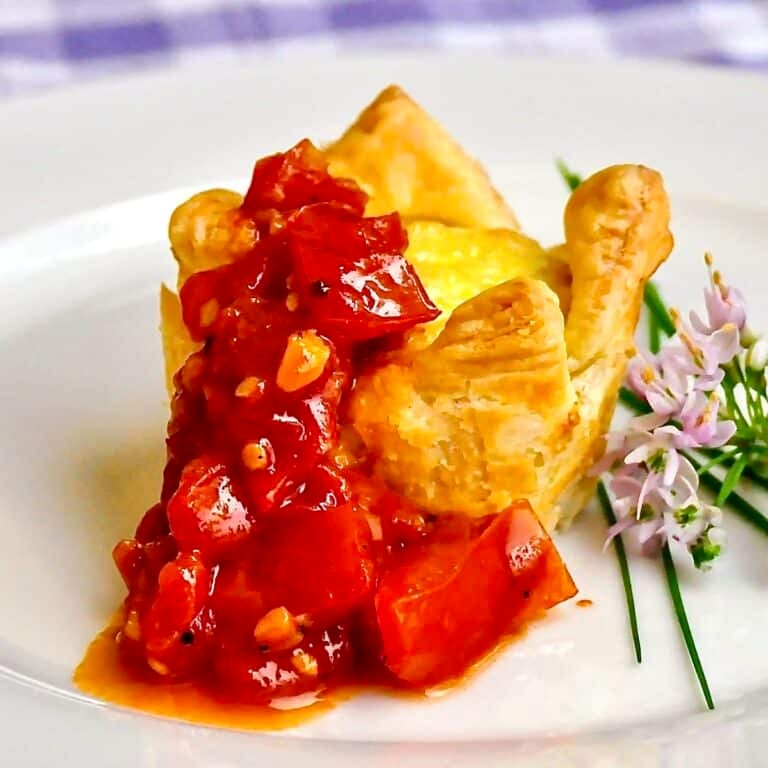 Parmesan Fennel Mini Quiche with Spicy Quick Tomato Compote. Close up photo of one serving on a white plate with chive flower garnish.