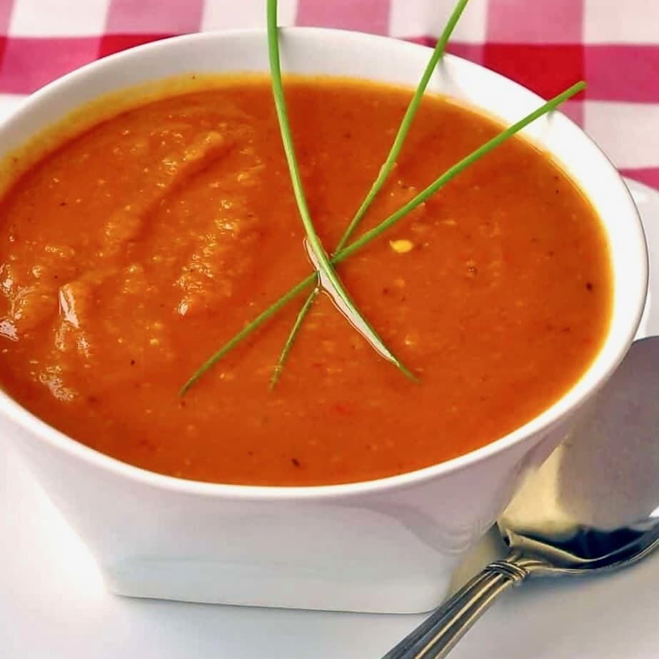 Close up photo of Roasted Squash and Red Pepper Soup in a white bowl with checkered tablecloth.