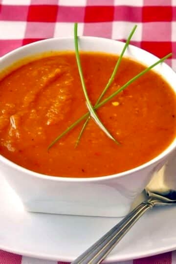 Roasted Squash and Red Pepper Soup in a white bowl with checkered tablecloth.