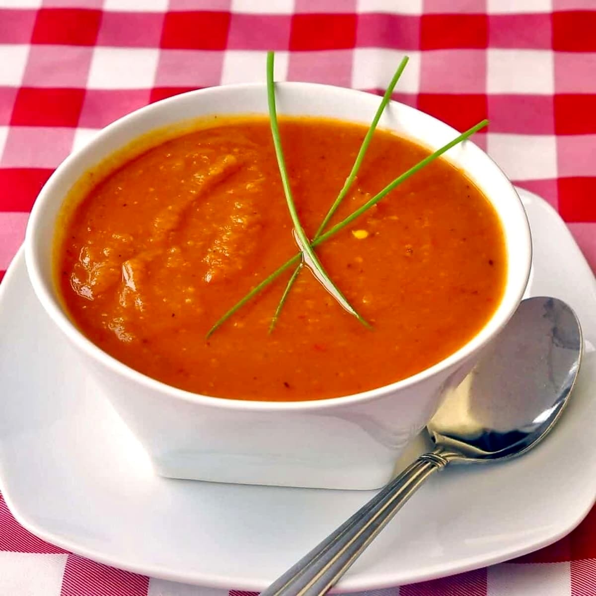 Roasted Squash and Red Pepper Soup in a white bowl with checkered tablecloth.