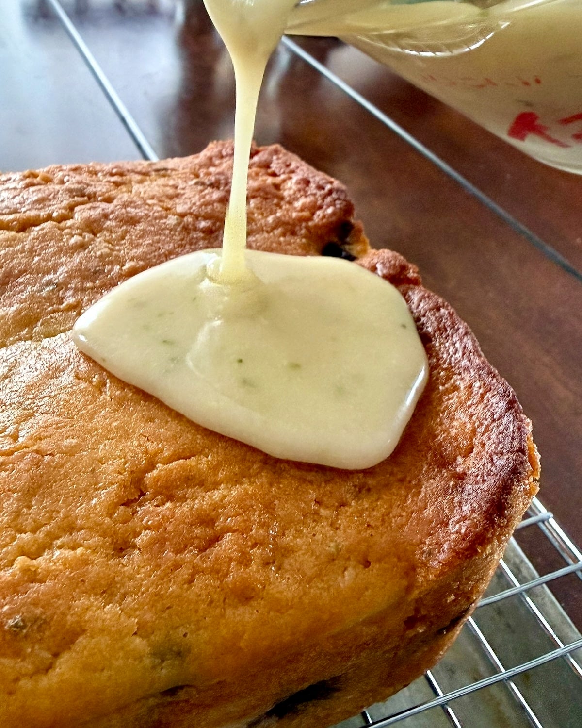 Close up photo of thick glaze being poured onto Glazed Blueberry Lime Loaf Cake.