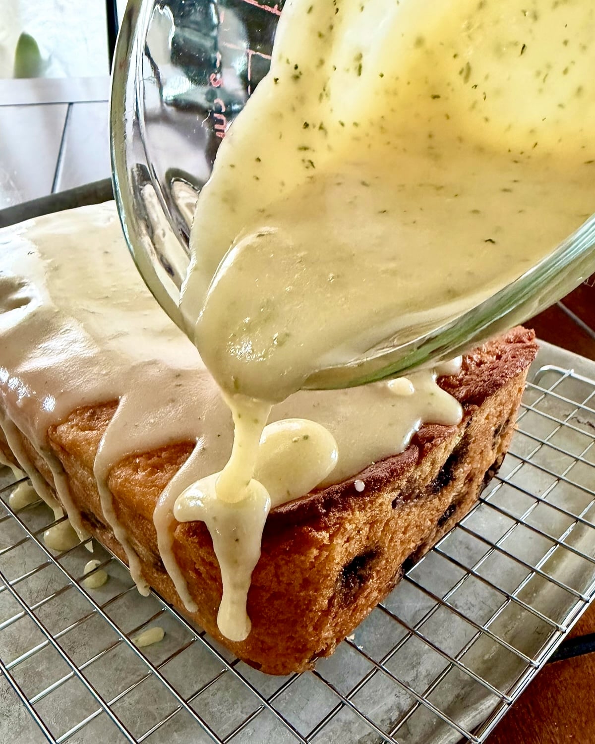 Thick glaze being poured onto Glazed Blueberry Lime Loaf Cake.