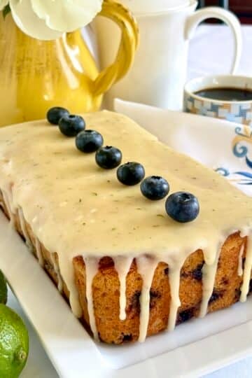 Photo of completed , uncut Glazed Blueberry Lime Loaf Cake on a white serving platter.