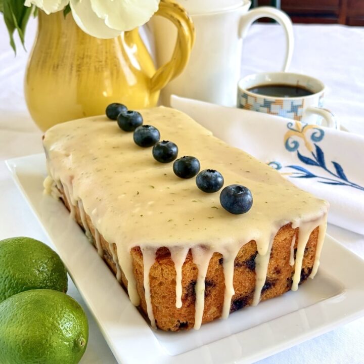 Photo of completed , uncut Glazed Blueberry Lime Loaf Cake on a white serving platter.