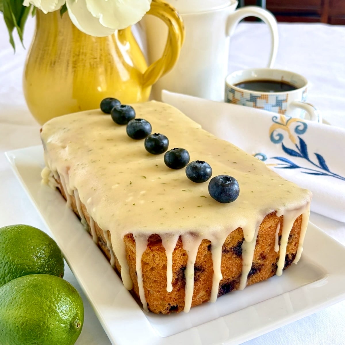 Photo of completed , uncut Glazed Blueberry Lime Loaf Cake on a white serving platter.