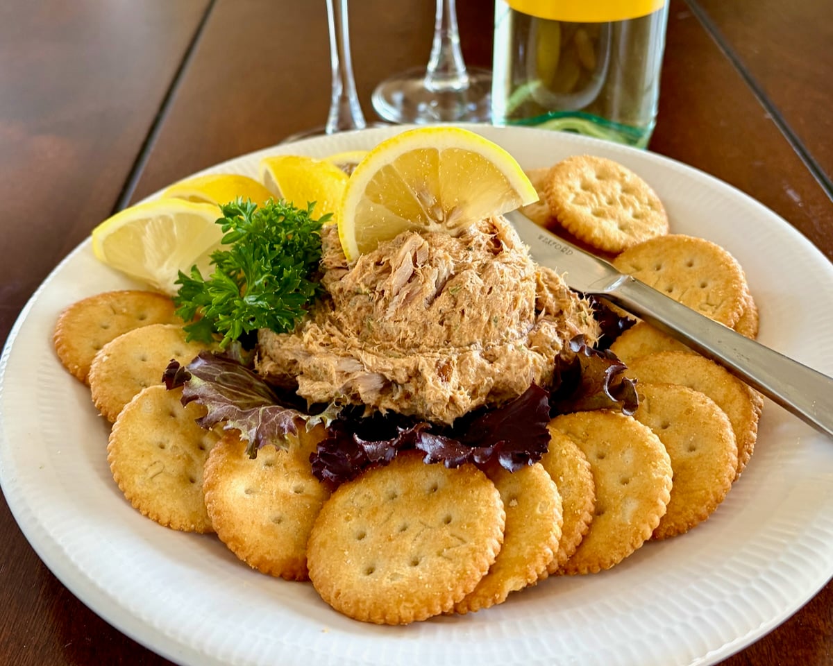 Wide shot photo shot of a scoop of Smoked Fish Dip served as an appetizer with lemon slices and Ritz Crackers on a white plate.