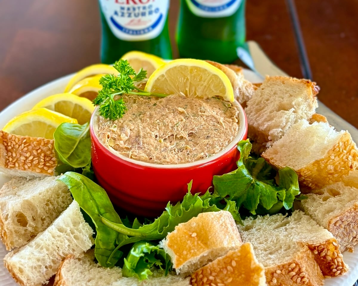 Wide shot photo of Smoked fish dip in a red ramekin with cold beer in the background