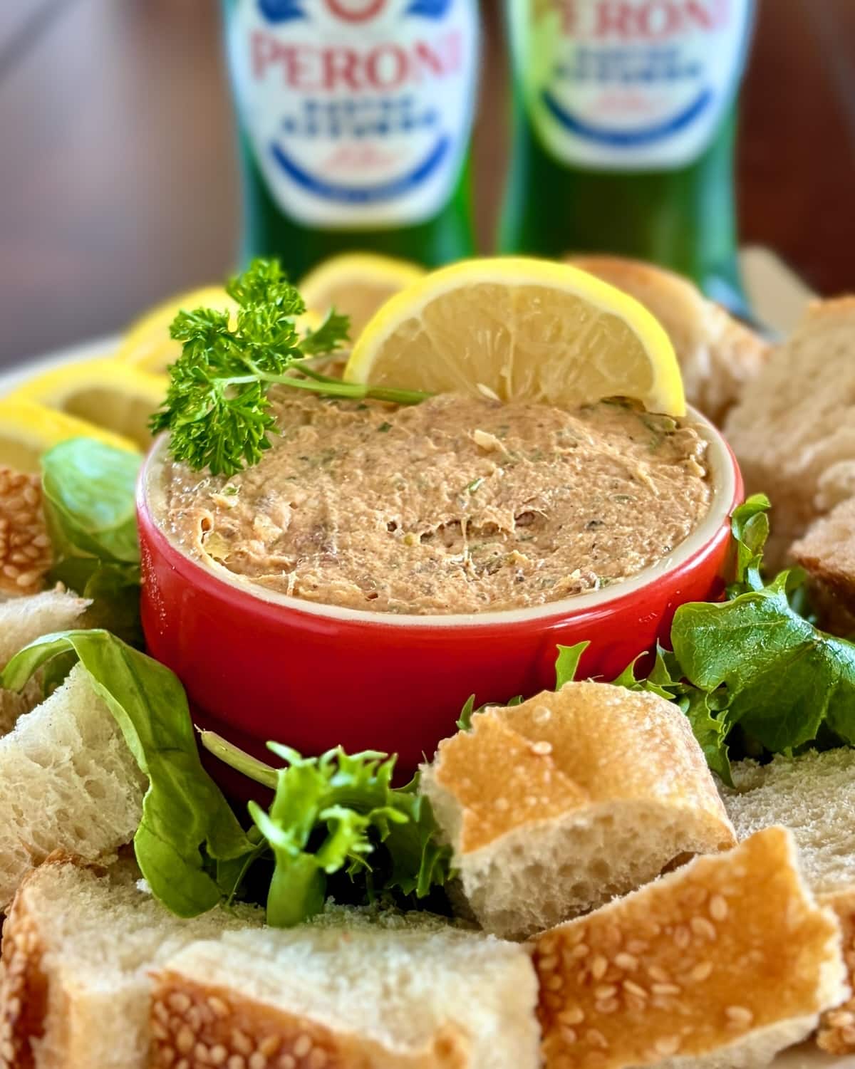 Close up photo of Smoked Fish Dip in a red ramekin with lemon slices, parsley and bread chinks.