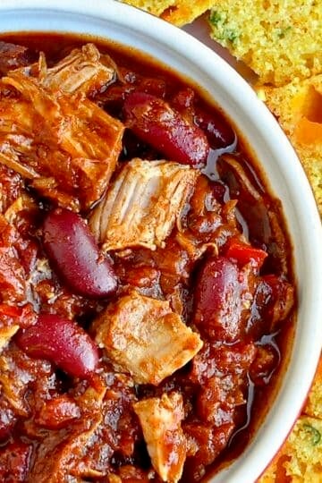 Pulled Pork Chili with Cheddar Green Onion Cornbread close up overhead photo of one serving in a white bowl.