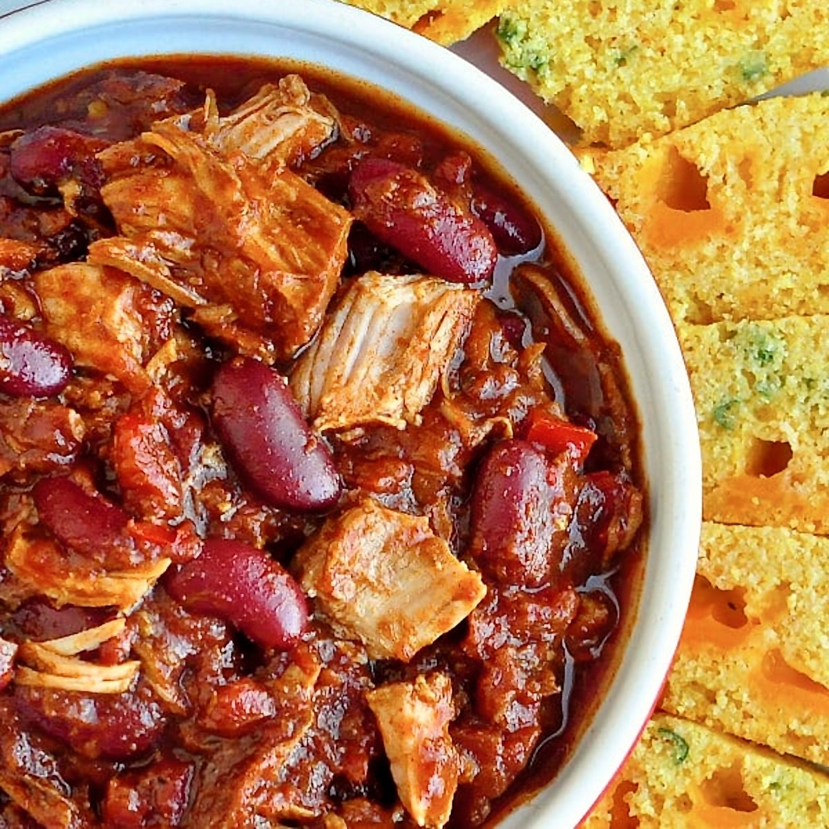 Pulled Pork Chili with Cheddar Green Onion Cornbread close up overhead photo of one serving in a white bowl.