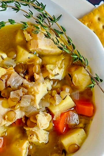 Chicken Thyme and Lentil Soup close up image of soup in a white bowl with crackers on the side