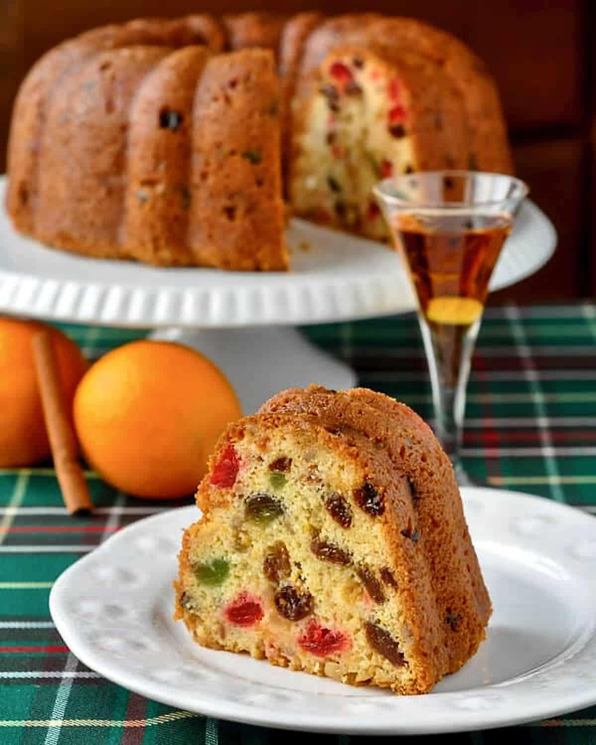 Orange Brandy Fruitcake photo of one slice on a white plate with a glass of orange brandy.