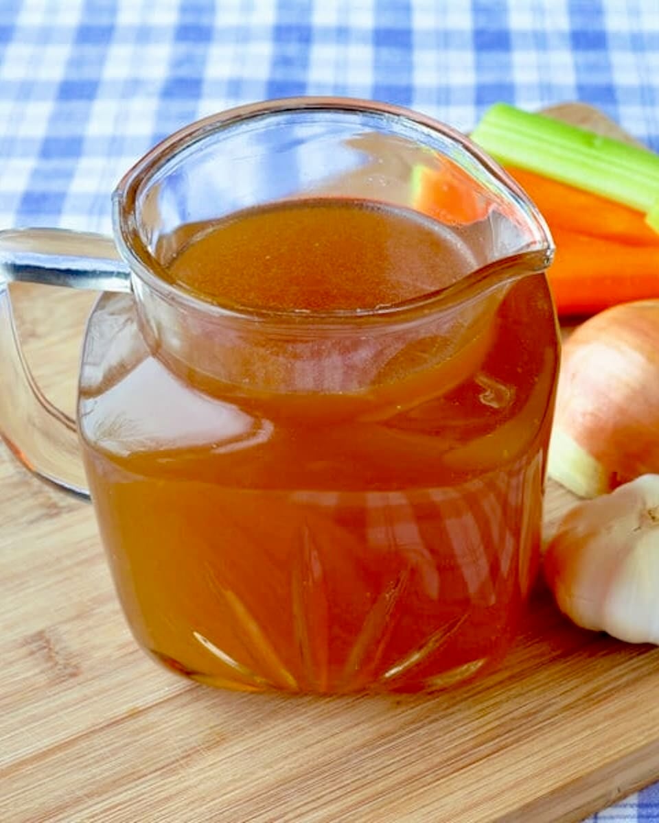 Close up photo of a vintage glass jug filled with stock and vegetables in the background. T