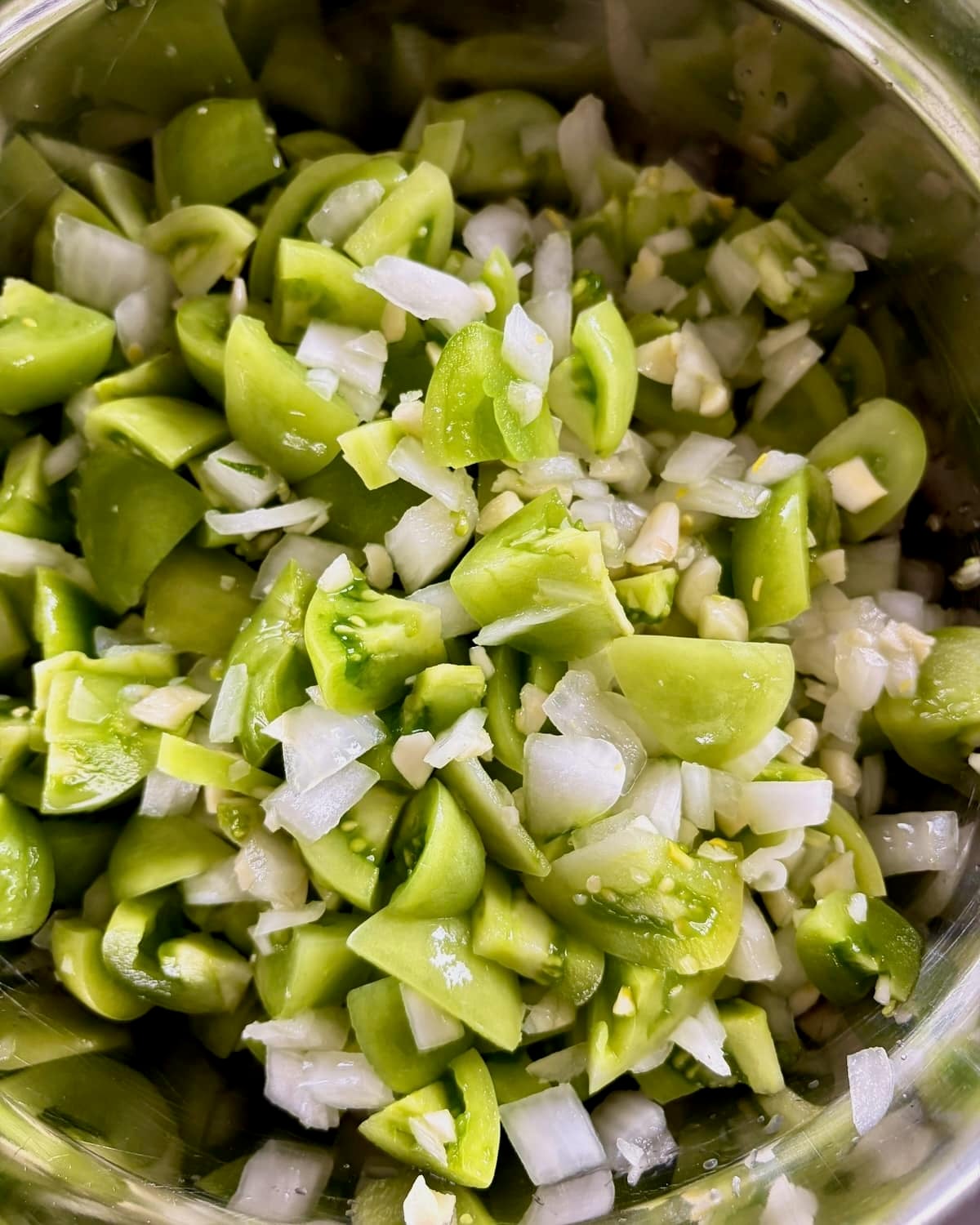 Photo of Chopped Green Tomatoes, onions and garlic in a stainless steel bowl.