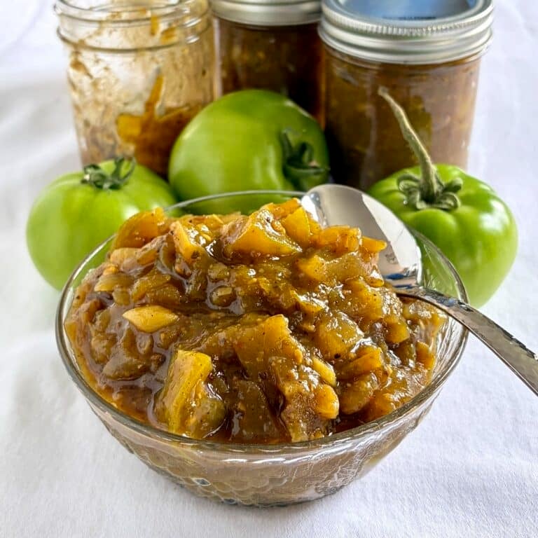 Close up photo of Photo of green tomato chow chow in a glass serving bowl with green tomatoes in the background for Google Featured Image.