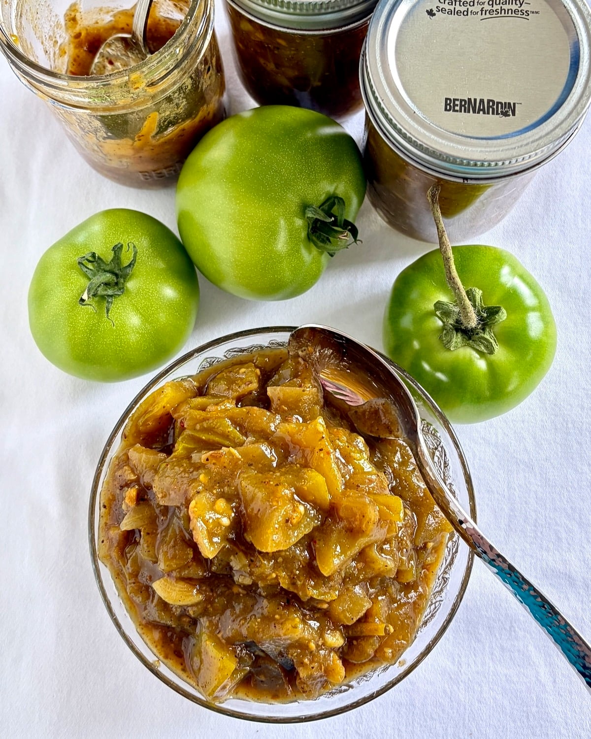 Overhead photo of Green Tomato Chow Chow in a glass serving dish surrounded by green tomatoes.