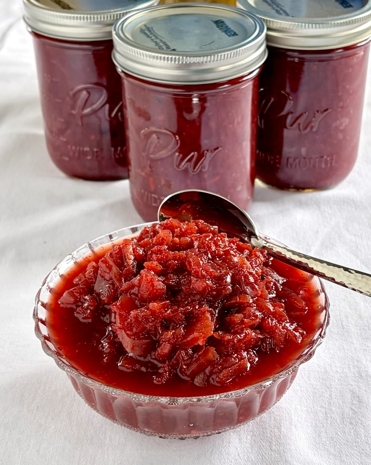 Easy Beet Relish close up photo served in a clear glass vintage bowl with bottles of relish in the background.