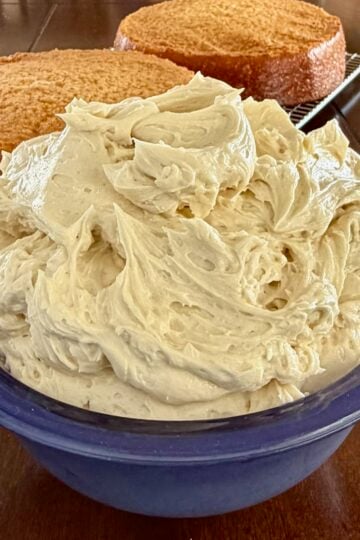 Close up Photo of Ermine Cream Frosting in a blue bowl with vanilla cake in the background.