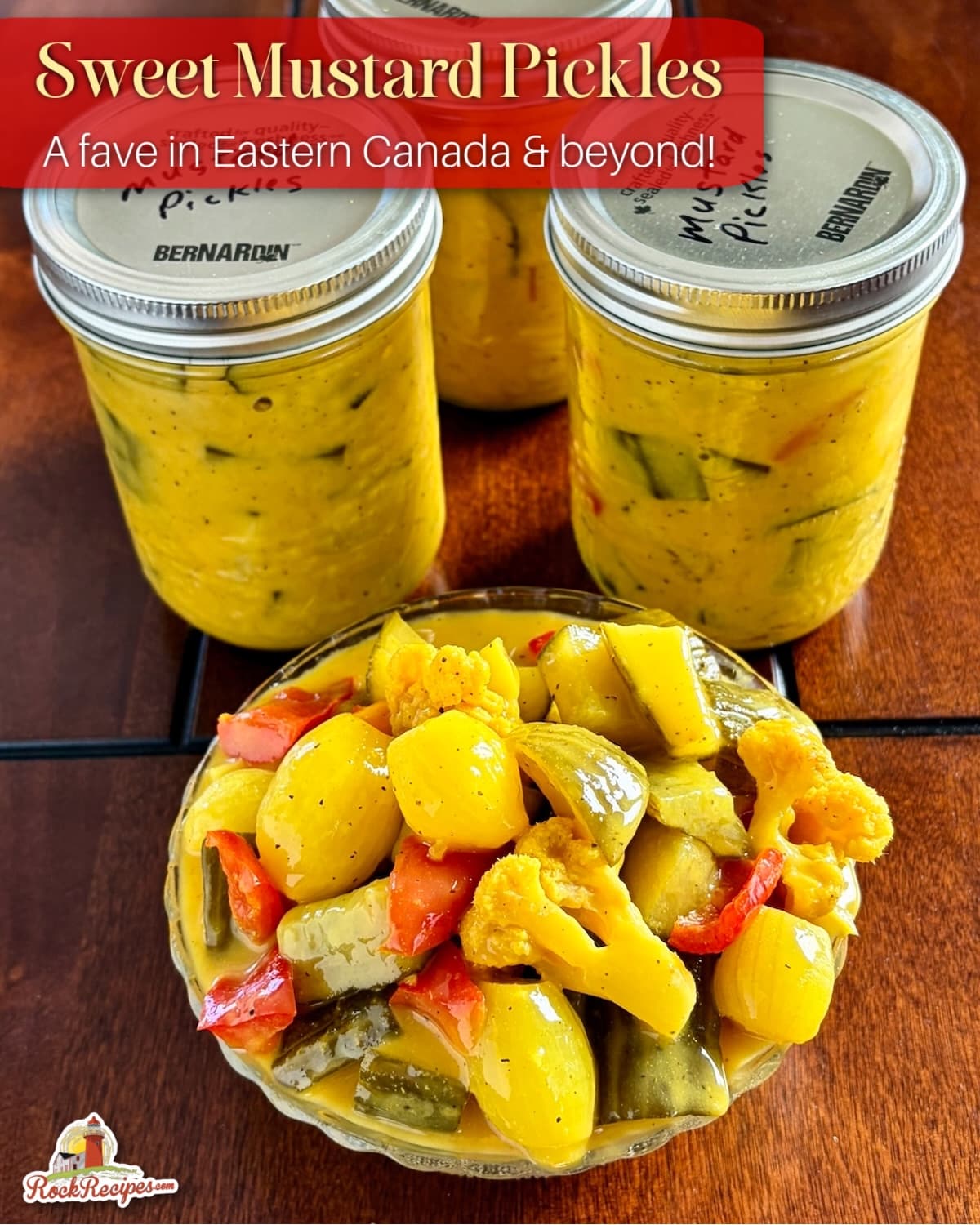 Newfoundland Mustard Pickles overhead shot photo of mixed pickles in an antique clear glass serving dish with bottles of finished pickles in the background with title text and Rock Recipes logo added for Pinterest and social media posts.