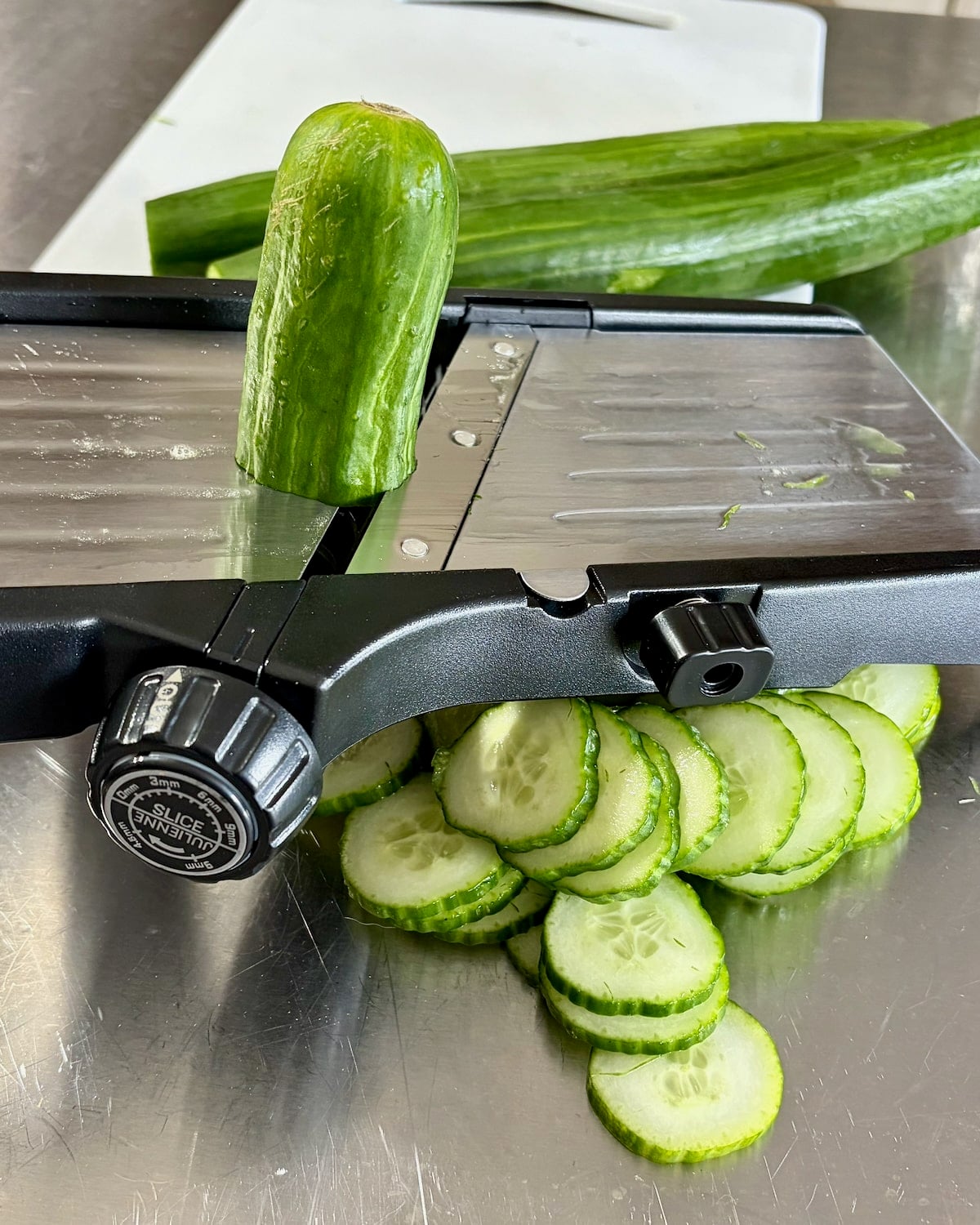 Photo if cucumbers being sliced on a mandolin.
