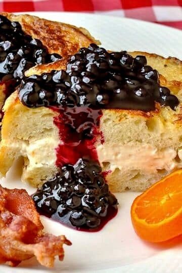 Cream Cheese Stuffed French Toast with Blueberry Sauce shown with bacon and orange slices on a white plate.