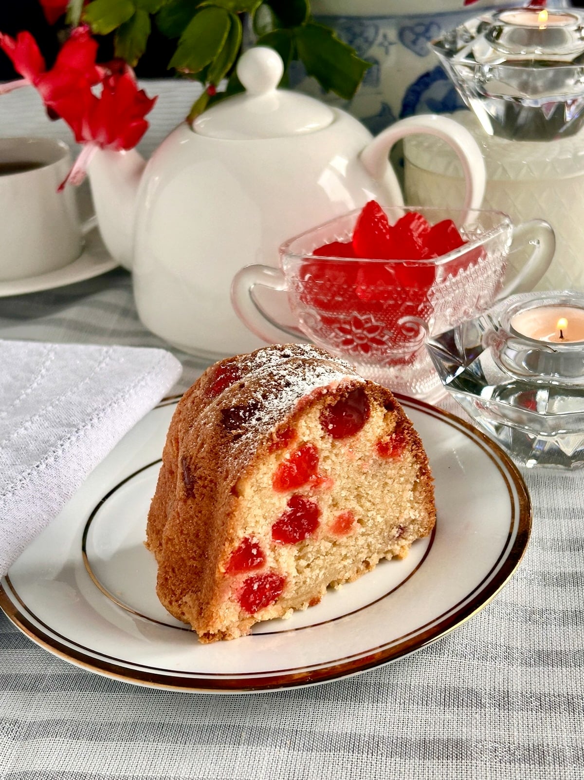 Wide shot photo of one slice of Swedish Berry Pound Cake with full cake and coffee service in the background formatted size for social media posts.