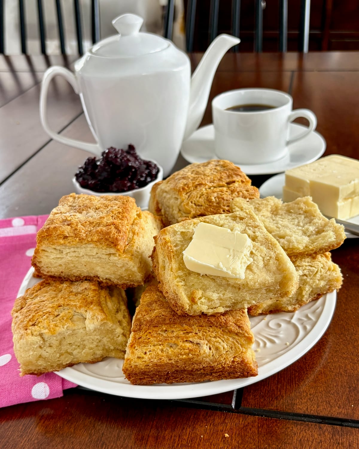 Flaky Sour Cream Biscuits on a white serving plate with one spread with butter.