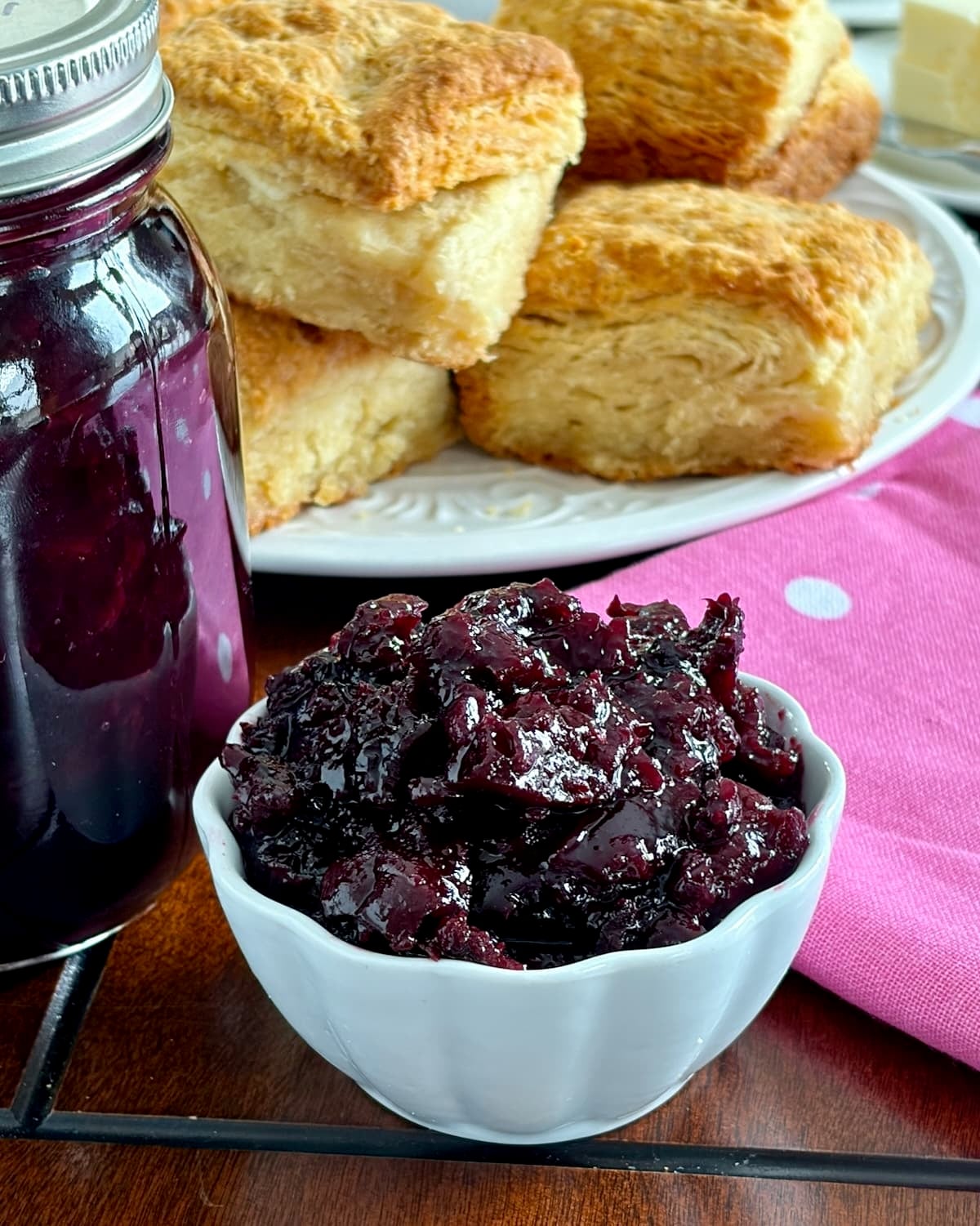 Low Sugar Blueberry Cherry Jam.in a white ramekin with sour cream biscuits in the background.