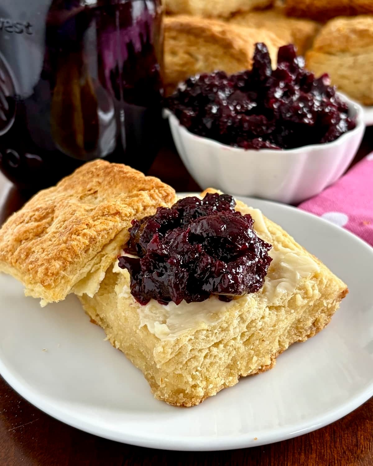 Low Sugar Blueberry Cherry Jam. on a sour cream biscuit with jam in background.