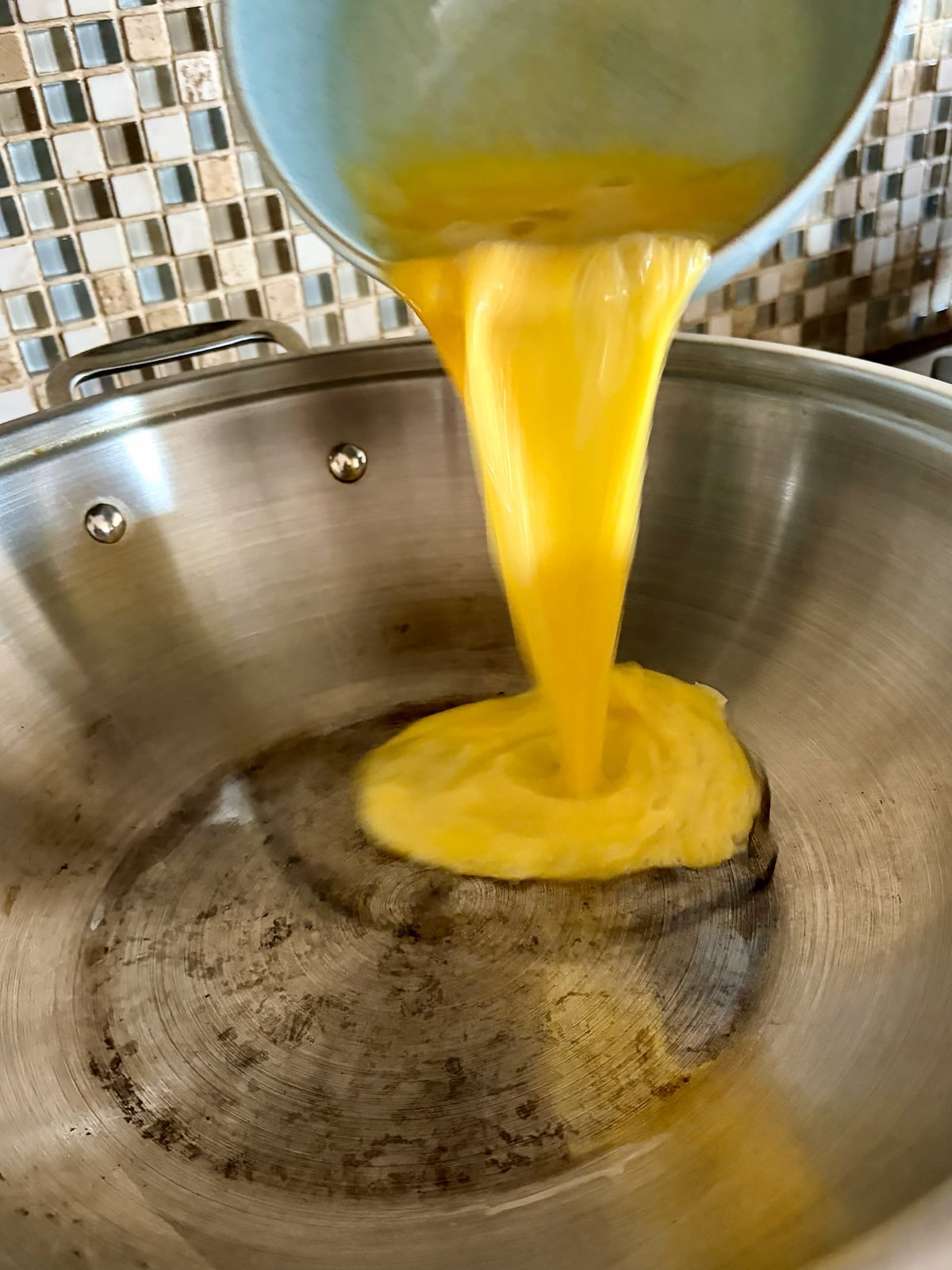 Photo of beaten egg being poured into a wok.